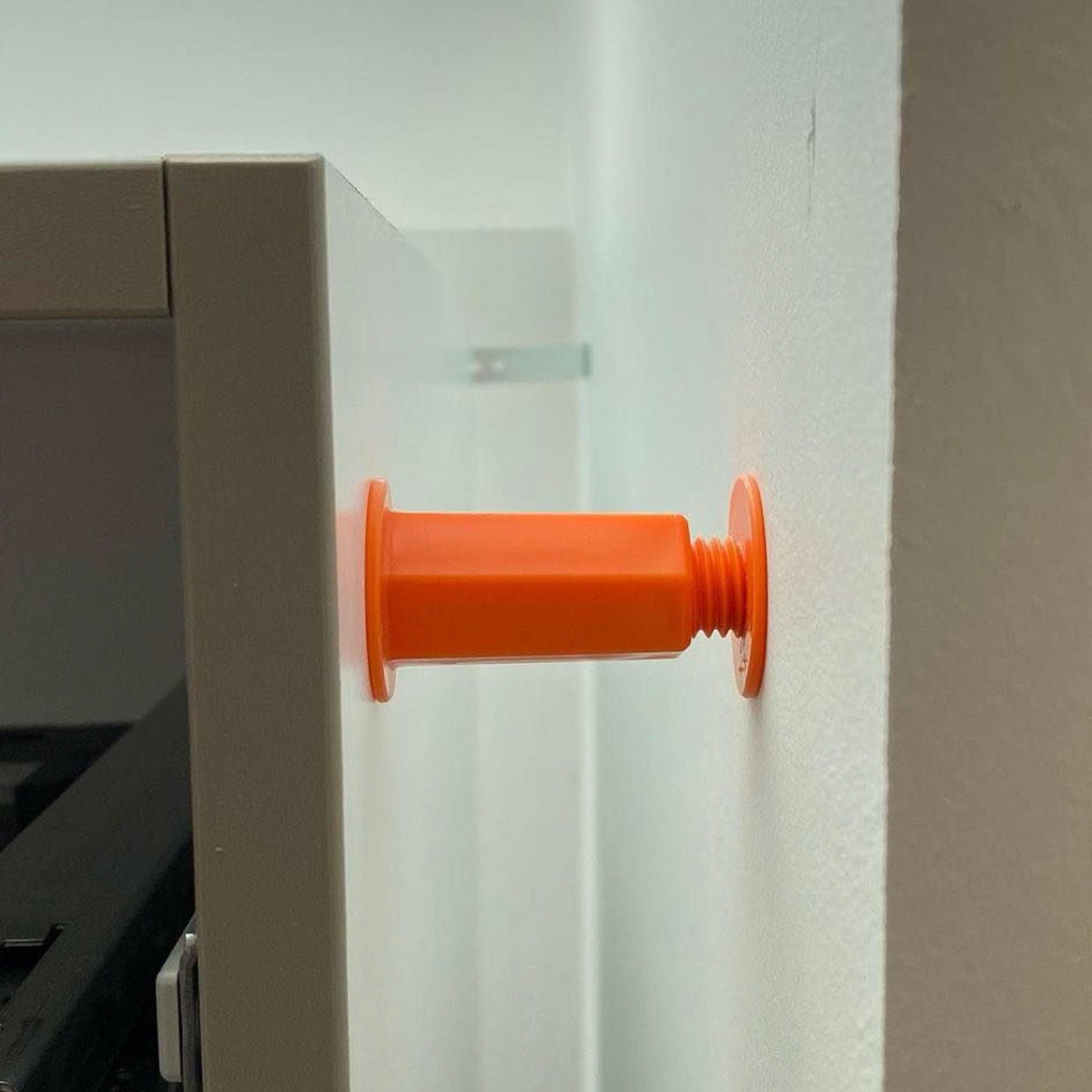 Space-Plug Regular orange installé entre un meuble de cuisine et un mur, illustrant un écart de fixation réglable pour une installation précise des meubles.