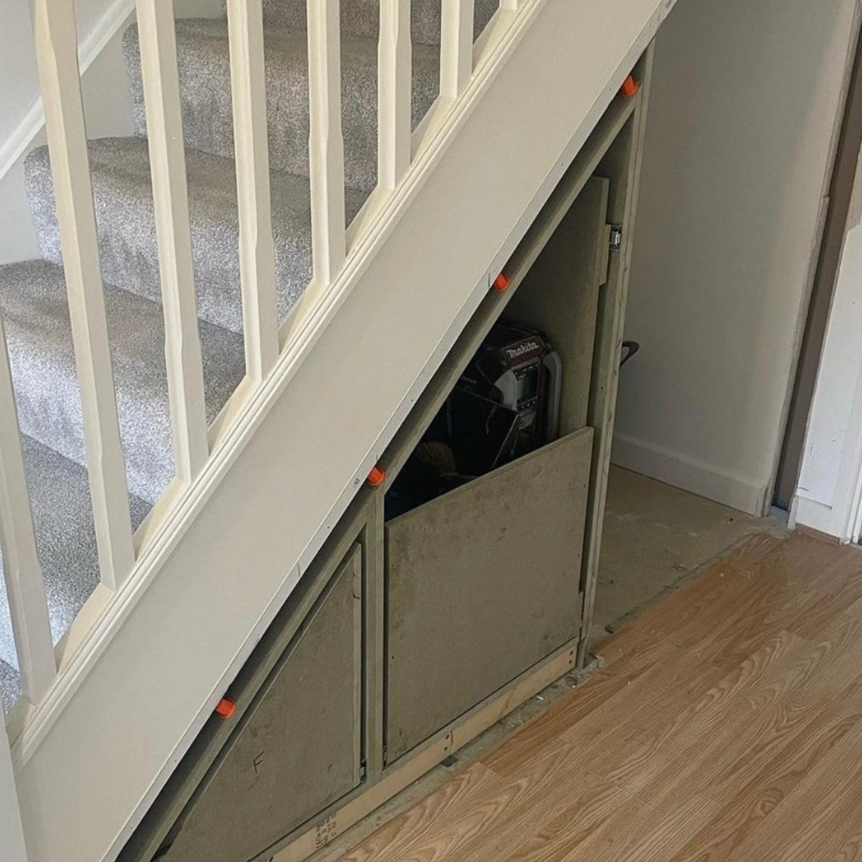 Meuble de rangement sous escalier installé avec des fixations réglables Space-Plug, utilisées pour compenser les irrégularités du mur et assurer un ajustement précis.